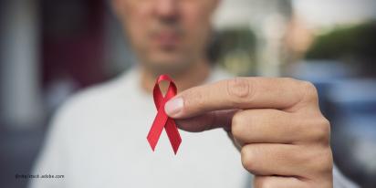 eine Person hält eine rote Schleife in der Hand in den Bildvordergrund