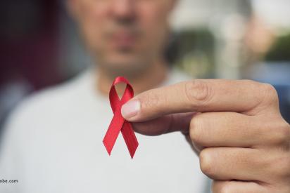 eine Person hält eine rote Schleife in der Hand in den Bildvordergrund