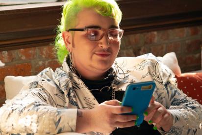 A genderqueer person looking at their phone
