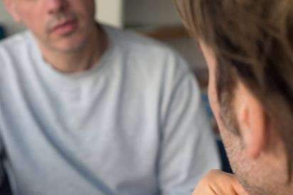 Zwei m&auml;nnlich gelesene Personen sitzen sich in einem ernsten Gespr&auml;ch gegen&uuml;ber.