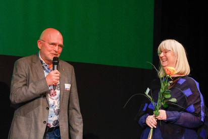 Mann mit Mikro und Frau mit Rose in der Hand stehen auf einer Bühne