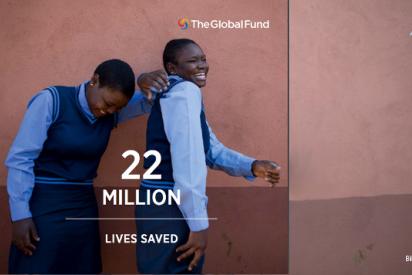 Zwei lachende Mädchen in Schuluniform stehen vor einer braunen Wand, davor der Text "22 million lives saved", oben das Logo des Global Fund.